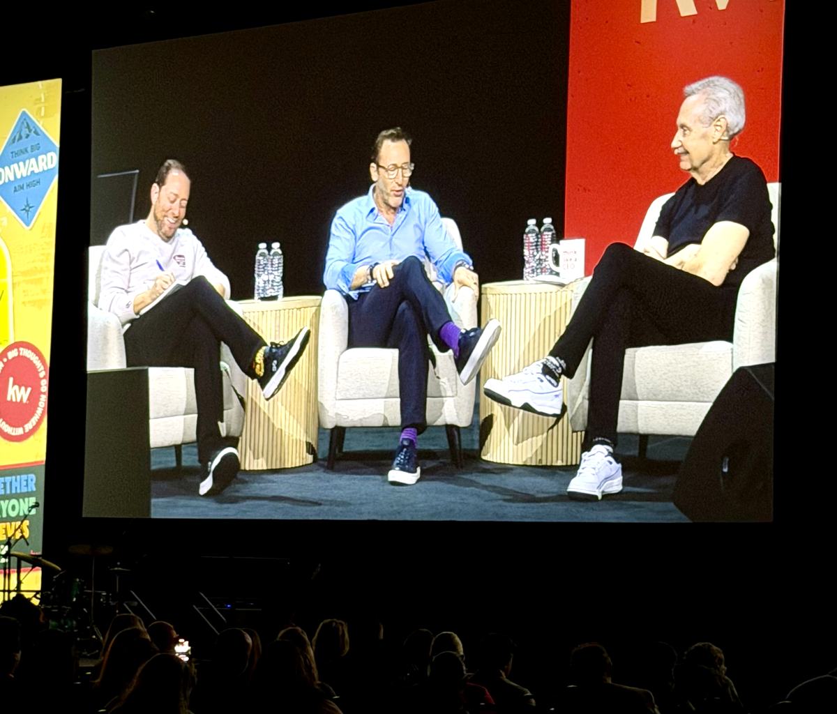 The three panelists on the main screen above rows of Mega Camp attendees
